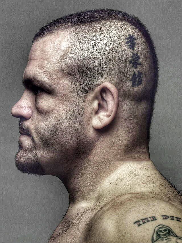 profile view of a man with a shaved head and tattoos on his head and shoulder.