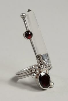 a closeup of a silver ring with a clear crystal and two garnet stones set into the metal. the crystal is shaped like a point and the garnets are round and oval. the ring is delicate and elegant.