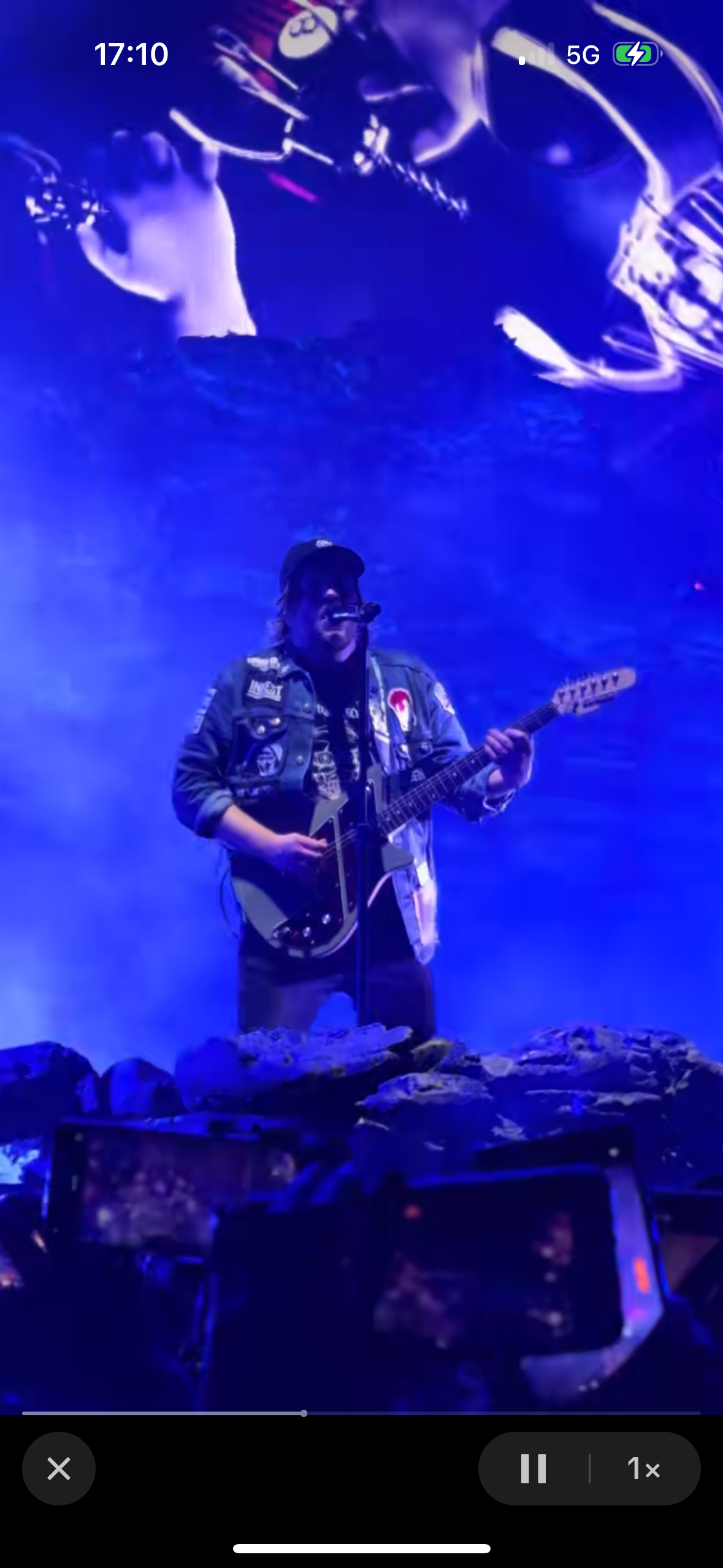 a rock and roll musician performing on stage at a concert. he is wearing a black leather jacket and is playing a black electric guitar. the stage is lit with blue light and the crowd is in the background, out of focus.