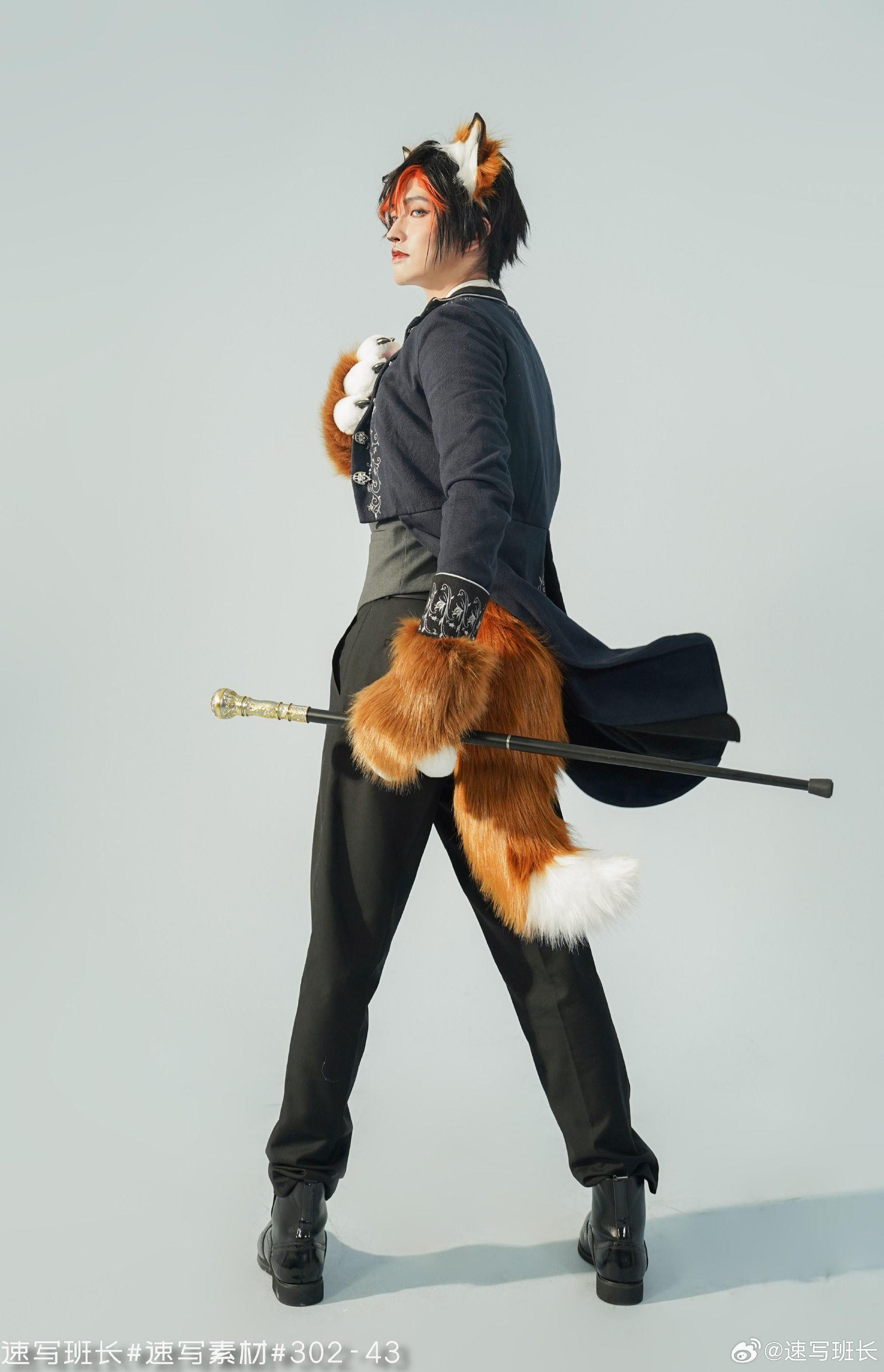 a man, facing away from the camera, stands in a studio setting. he is wearing a fox costume complete with ears, tail, and pawlike gloves. the costume incorporates a formal attire aesthetic with a dark blue jacket and black pants. he holds a cane in his right hand.  the lighting is bright and evenly distributed, highlighting the details of the costume. the background is a solid light blue, minimizing distractions and emphasizing the subject.