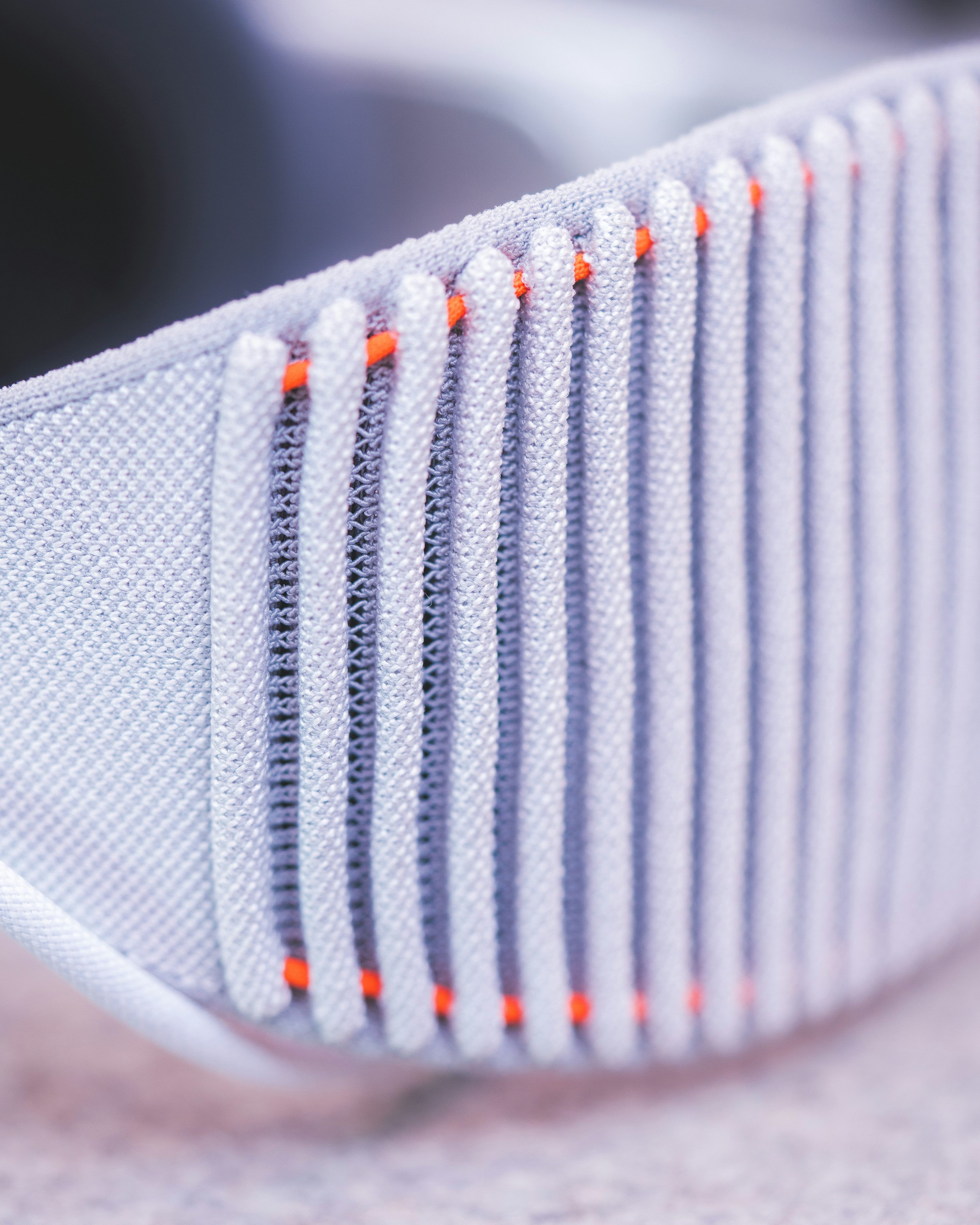 a closeup shot of the fabric and mesh of a gray shoe with orange vertical lines running through it.