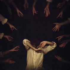 a person is surrounded by many hands reaching towards them in a dark and shadowy environment. the figure appears vulnerable and helpless, creating a sense of anxiety and fear. the hands are silhouetted against the darkness, making them appear menacing.
