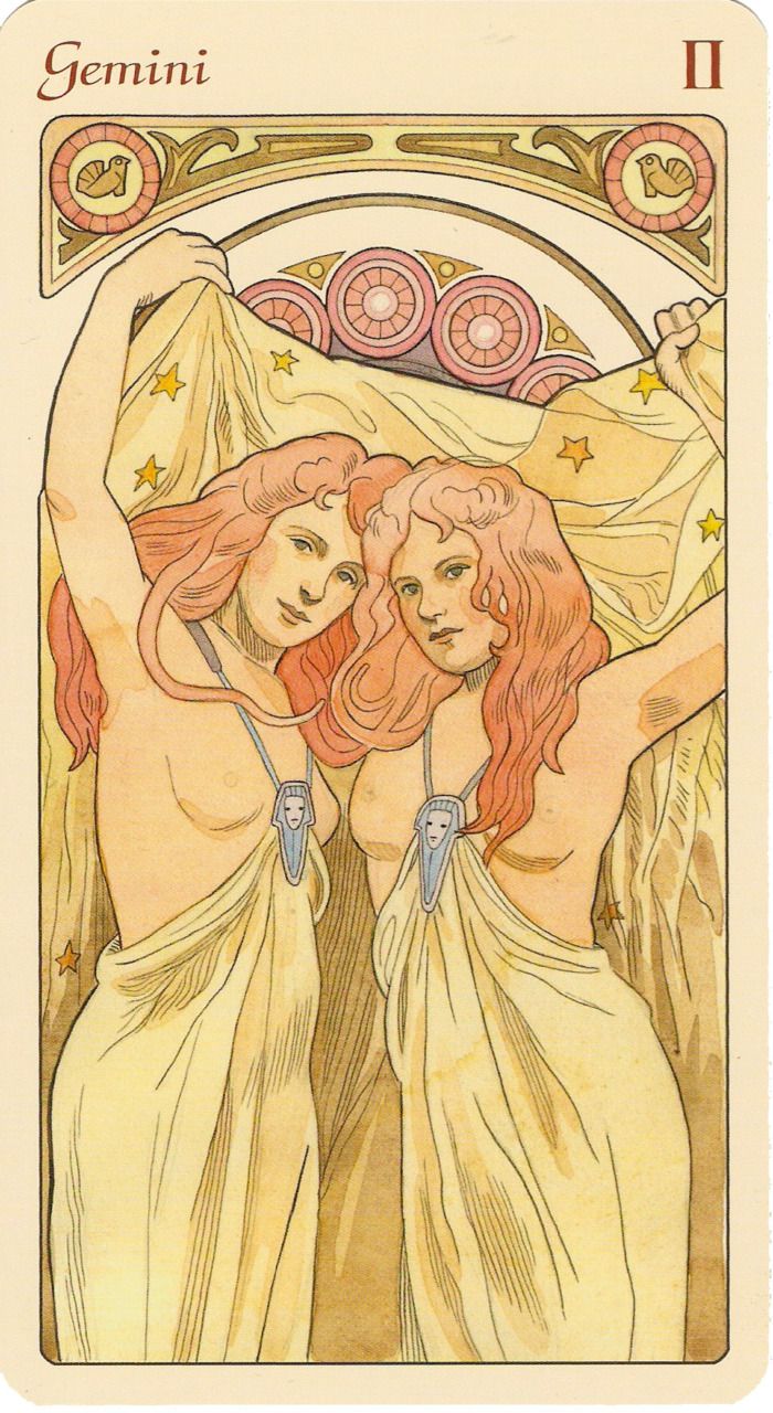 this is an illustration of the gemini tarot card, featuring two nude women standing sidebyside, draped in golden cloth adorned with stars. they each wear a necklace with a face pendant. above them is an arch design with decorative circles and a zodiac symbol, and the card is titled "gemini" with the roman numeral "ii".