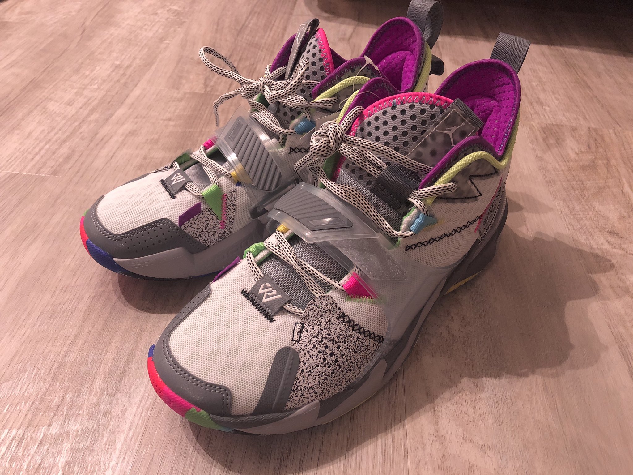 a pair of grey, pink, blue and green nike jordan sneakers on a wood floor.