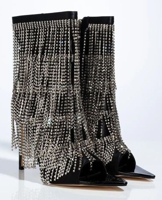 the image shows a pair of black, opentoe stiletto boots completely covered in layers of silver rhinestones. the rhinestones form a fringelike cascade that covers the majority of the boots. they appear to be standing on a reflective white surface. the boots have a sleek, pointed opentoe design, and stiletto heels.