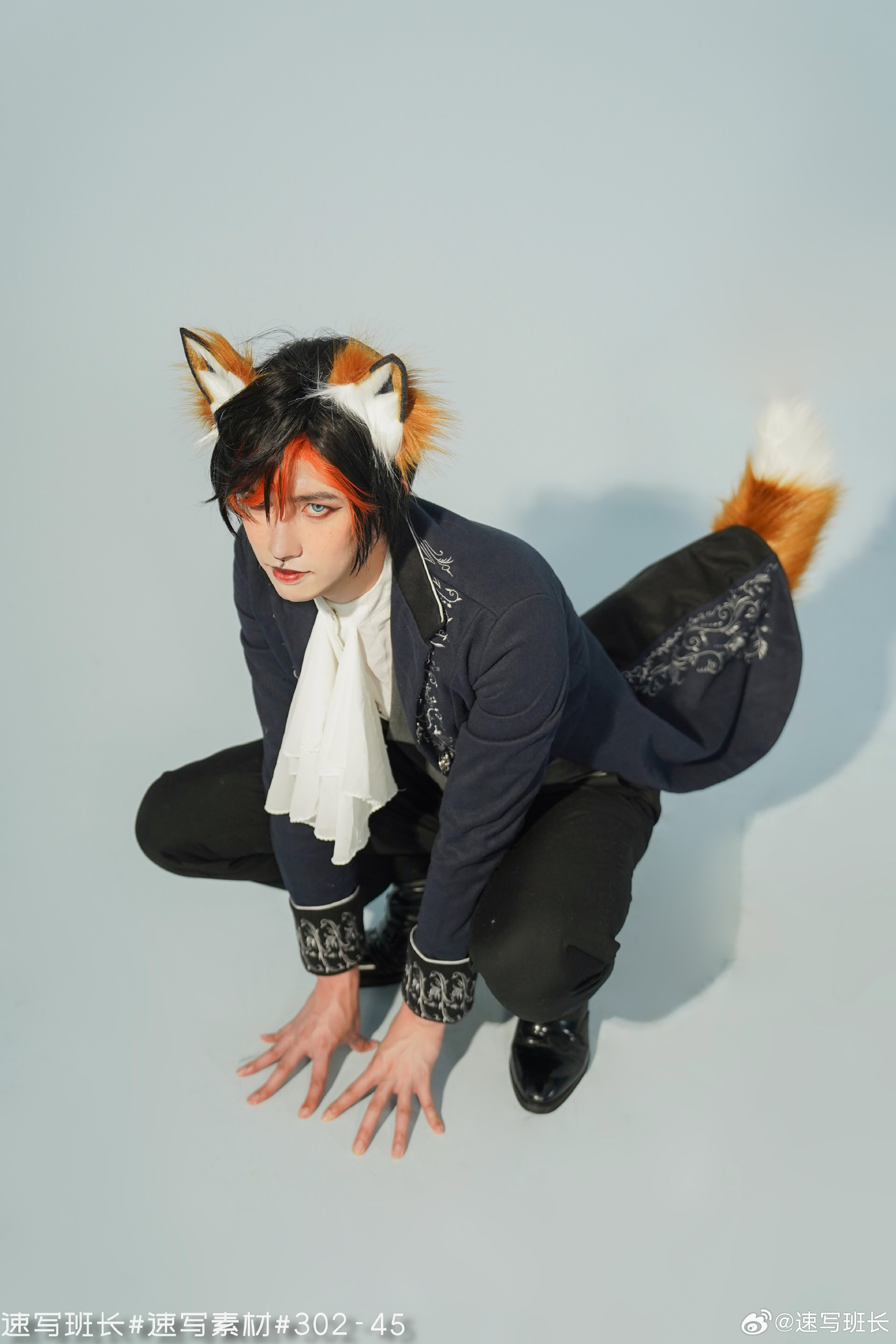 a man in a blue and white cosplay outfit with fox ears and tail. he is crouching in a studio, looking up at the camera.  the image has studio lighting and a low angle perspective. there is chinese text at the bottom of the image.