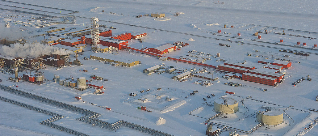 an aerial view of an oil rig in a snowy winter landscape. the rig is a complex industrial facility with many buildings, pipes, and tanks. it is located in a remote, arctic area. the snow covers everything, making the landscape look white and barren. the rig is a symbol of the oil and gas industry, and it is a reminder of the importance of this industry to the world economy.