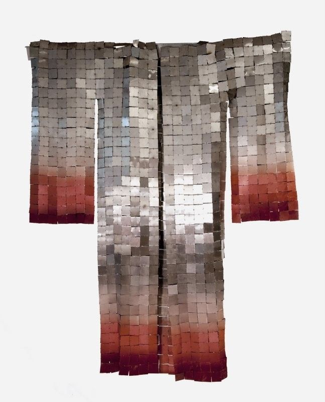 a fulllength image showcases a handmade kimonolike sculpture, composed of interconnected metal squares. the squares transition from a metallic gray at the top to a reddish hue at the bottom, creating a gradient effect. the garment, with its wide sleeves and traditional shape, is artistically displayed, emphasizing its textilelike quality and design.