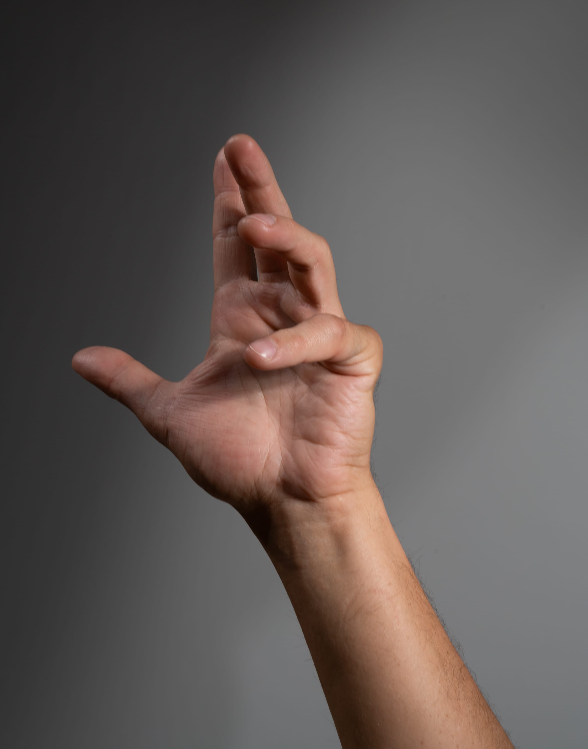 the image shows a right human hand with fingers spread and reaching upwards against a gray background. the hand is lit by artificial light.