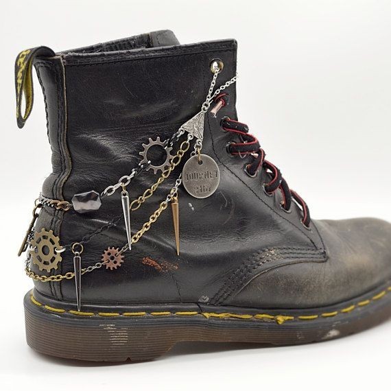 a closeup shot of a wellworn black dr. martens boot adorned with various steampunkinspired jewelry.  multiple chains with gear charms, spikes, and small metal pendants are attached to the boot, creating a layered and customized look. the boot shows signs of age and wear, adding to its character.  the background is plain white, focusing the attention on the boot and its embellishments.