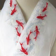 a closeup image of the collar of a white garment with delicate red fish embroidery. the fabric is sheer and the embroidery is detailed, creating a beautiful and elegant design. the background is white and the image is focused on the embroidery.