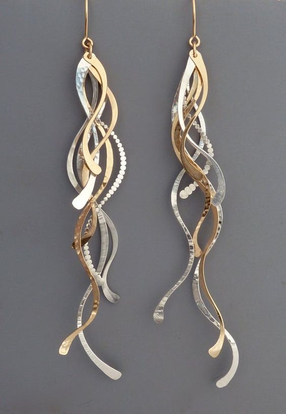 a pair of dangling earrings made of swirling gold and silver metal. the earrings are photographed against a gray background.