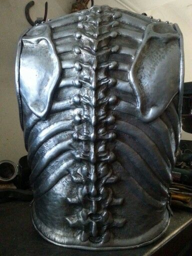 the image shows the back view of a sculpted piece of metal armor. the armor is designed to look like a rib cage, with individual ribs crafted in detail. the armor is made of a dull gray metal and appears to be quite heavy.