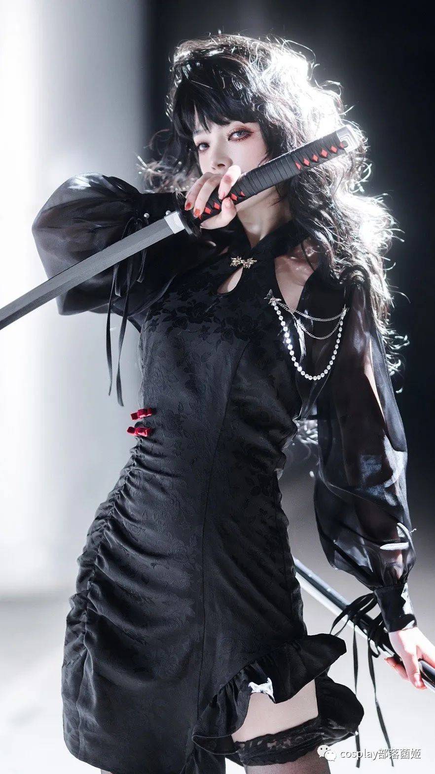 a woman in cosplay is posing with a katana. she's wearing a black gothicstyle dress with lace details, ruffles, and ribbons. she has fair skin, wavy hair with bangs, and red nail polish. she also wears black stockings, a string of pearls, and black arm warmers or cuffs. she holds the katana with both hands, and the scene is illuminated with bright lighting.