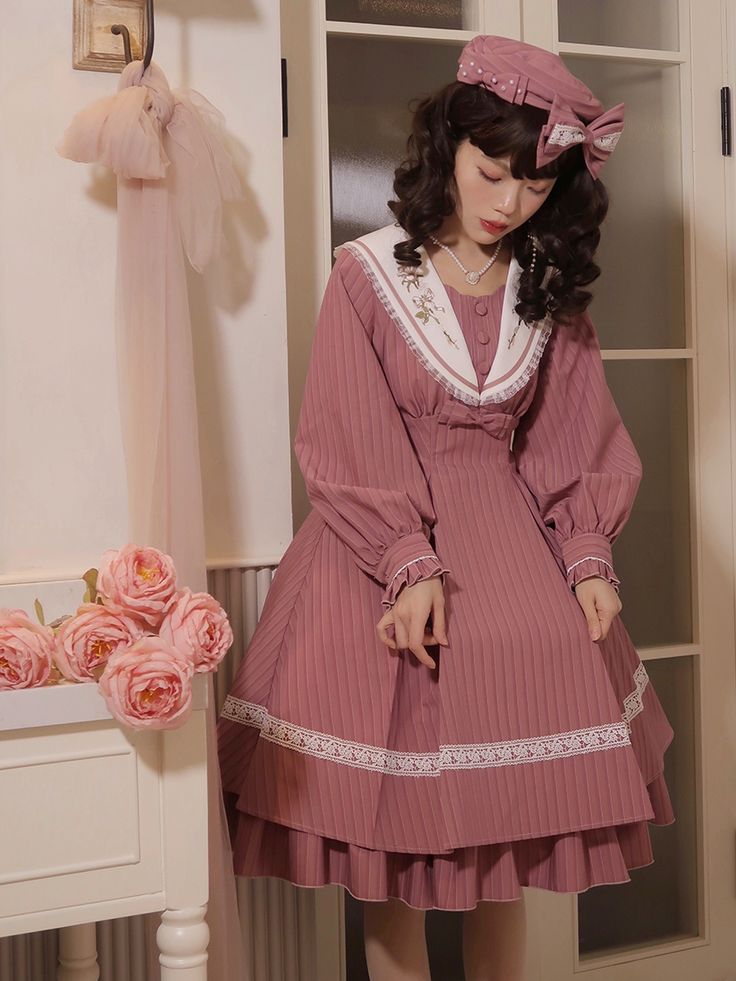 a young woman is posing in a pink lolita fashion dress. the dress has a sailor collar and white lace trim. she is also wearing a matching beret. the photo is taken indoors in a room with soft, natural lighting.