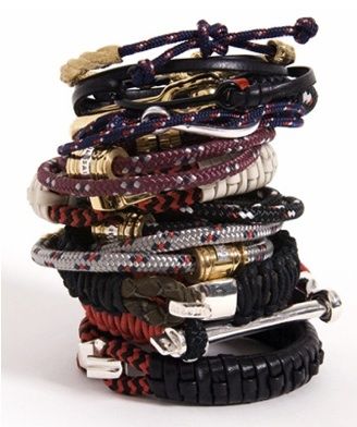 a stack of bracelets in various colors and styles, including braided rope bracelets, leather bracelets, and metal accents. the bracelets are stacked on top of each other and create a visually appealing display of texture and color. the bracelets are likely to be a fashion accessory for someone who enjoys a bohemian or nautical style.