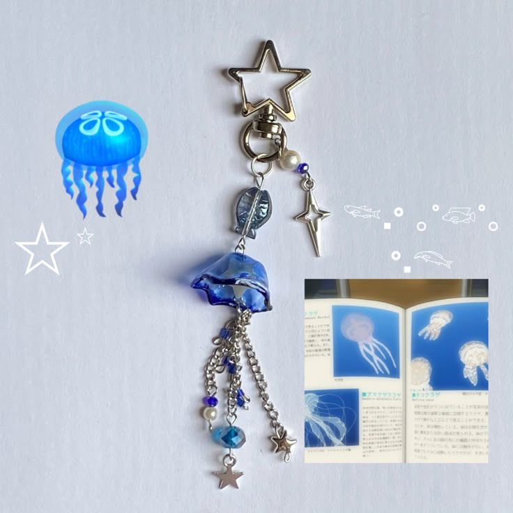 the image features a jellyfishthemed keychain with a star clasp, dangling from a silver ring. the main charm is a blue jellyfish figurine, complete with silver chains and beads representing the tentacles. a silver leaf charm and a star charm dangle above the jellyfish, while a small pearl and a silver starshaped pendant are attached to the main ring. a book with jellyfish illustrations is also visible in the image. there is also a digitally added jellyfish, a line art star, and line art fishes and circles. the image is on a white background.