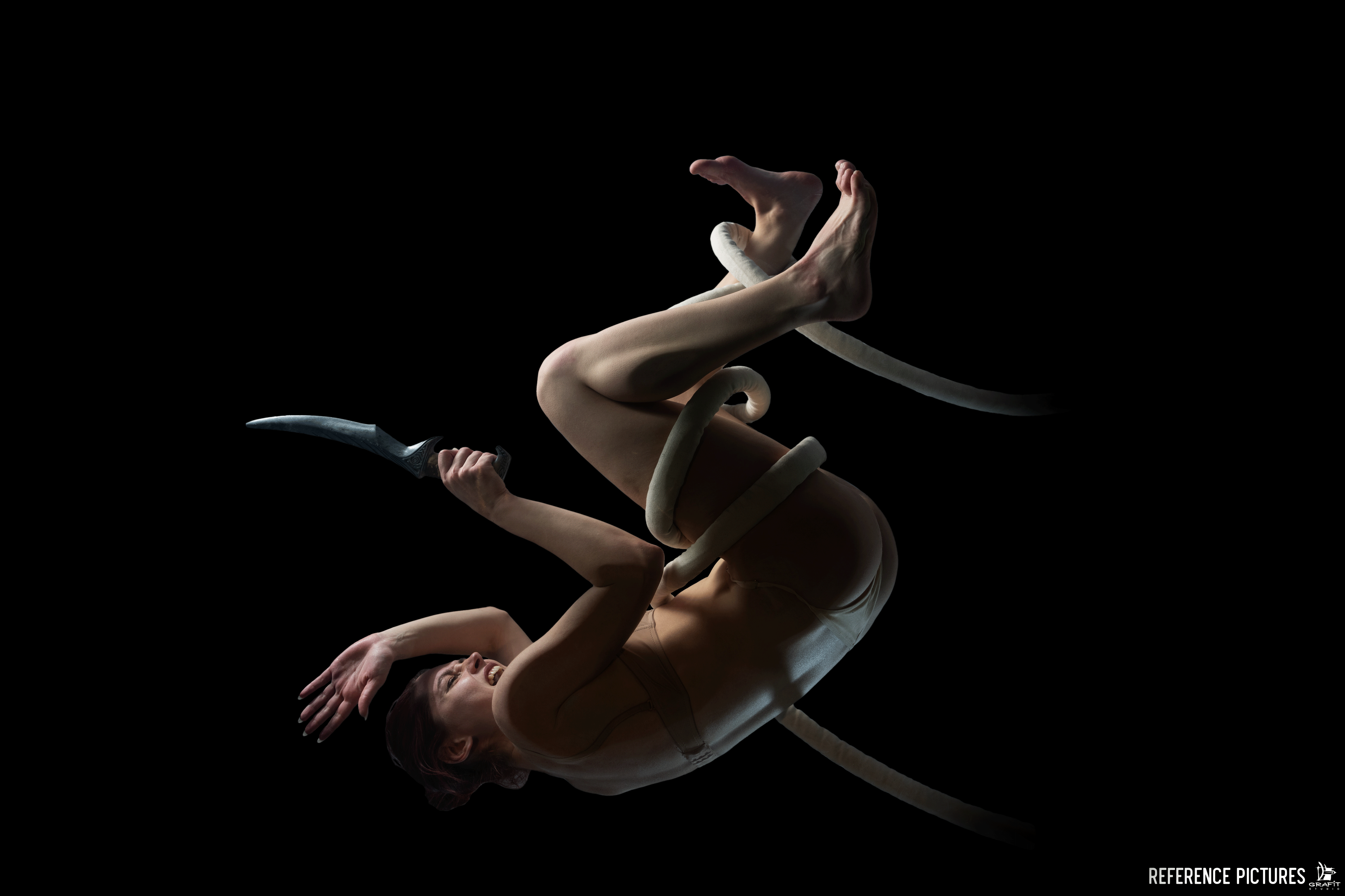 a woman is captured midfall against a stark black background. she is wearing a bodysuit and clenching a knife in her right hand. a thick white rope is wrapped around her body. her facial expression suggests terror or fear. the dramatic lighting emphasizes the motion and emotion of the scene.