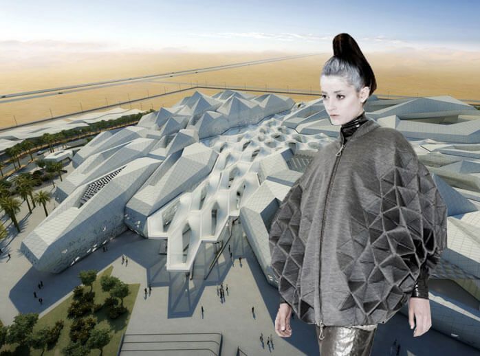 a woman in a grey, geometricallydesigned jacket stands in front of a futuristic building.  the building has a gray, geometric design with sharp angles. the woman's jacket is a contemporary, bold style and matches the architecture. the background is a sandy, desert landscape.