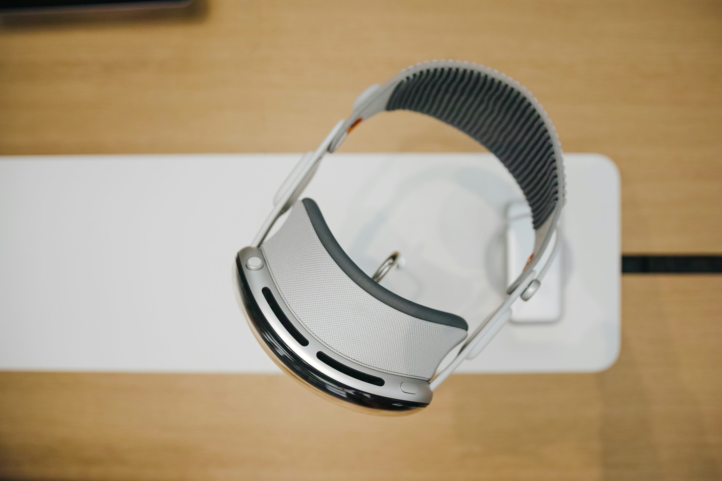 a closeup shot of an apple vision pro vr headset resting on a white stand, showing its silver and black design.