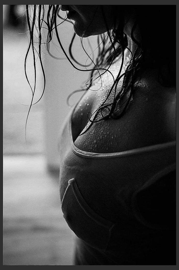 the image is a black and white closeup portrait of a woman's upper body.  she is positioned in a side profile, her wet, dark hair cascading down her shoulders and chest. the lighting creates a dramatic contrast, highlighting the droplets of perspiration on her skin.  she is wearing a darkcolored sports bra, and the overall mood of the photo is sensual and intimate. the focus is on the texture of her skin and hair, as well as the interplay of light and shadow.