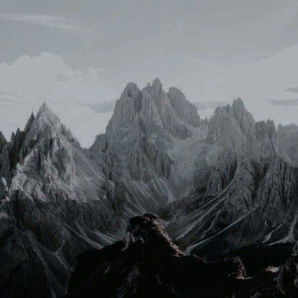 the image shows a landscape of jagged, rocky mountains under a cloudy, overcast sky. the scene is dominated by the peaks and ridges of the mountains, rendered in shades of gray and dark tones. the overall impression is one of ruggedness and imposing natural beauty.