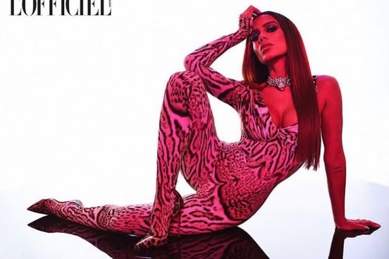 a photograph of anitta wearing a pink and black leopard print jumpsuit, jewelry, and posing on a reflective surface under red lighting for the cover of l'officiel magazine.