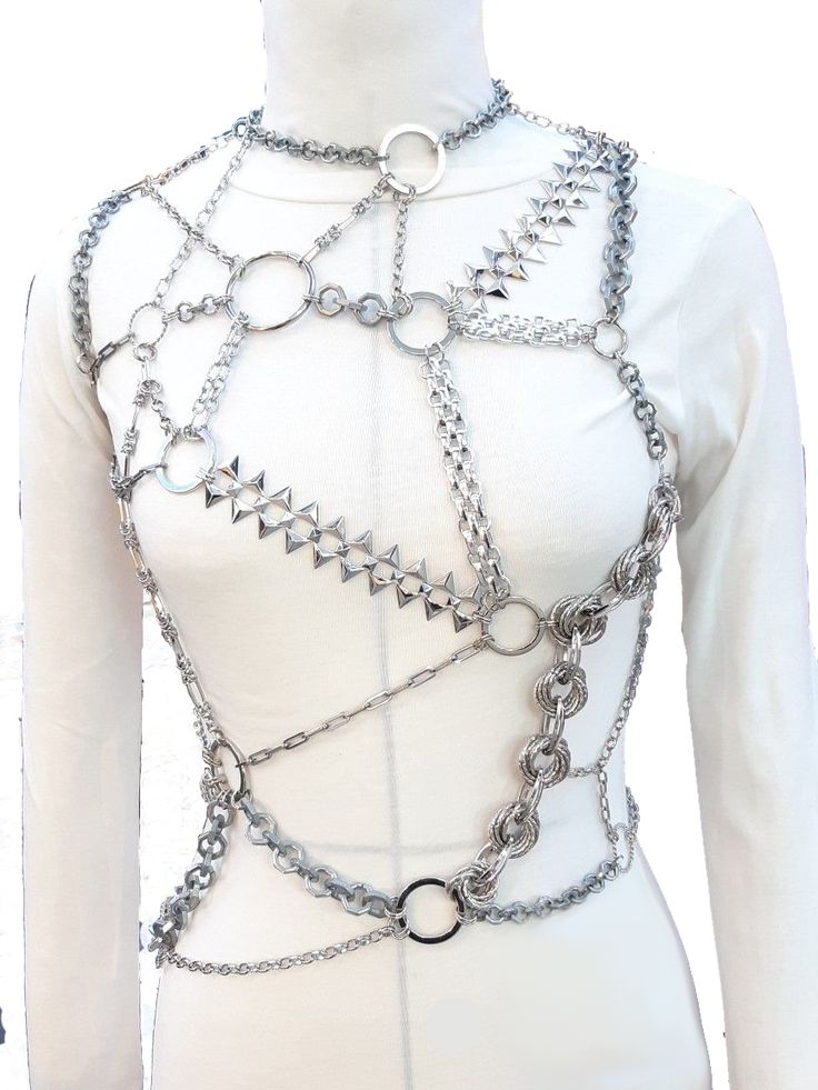 a mannequin wearing a silver chain body harness over a longsleeved white shirt. the harness consists of various types of chains and rings, including a spiked chain and a collar.