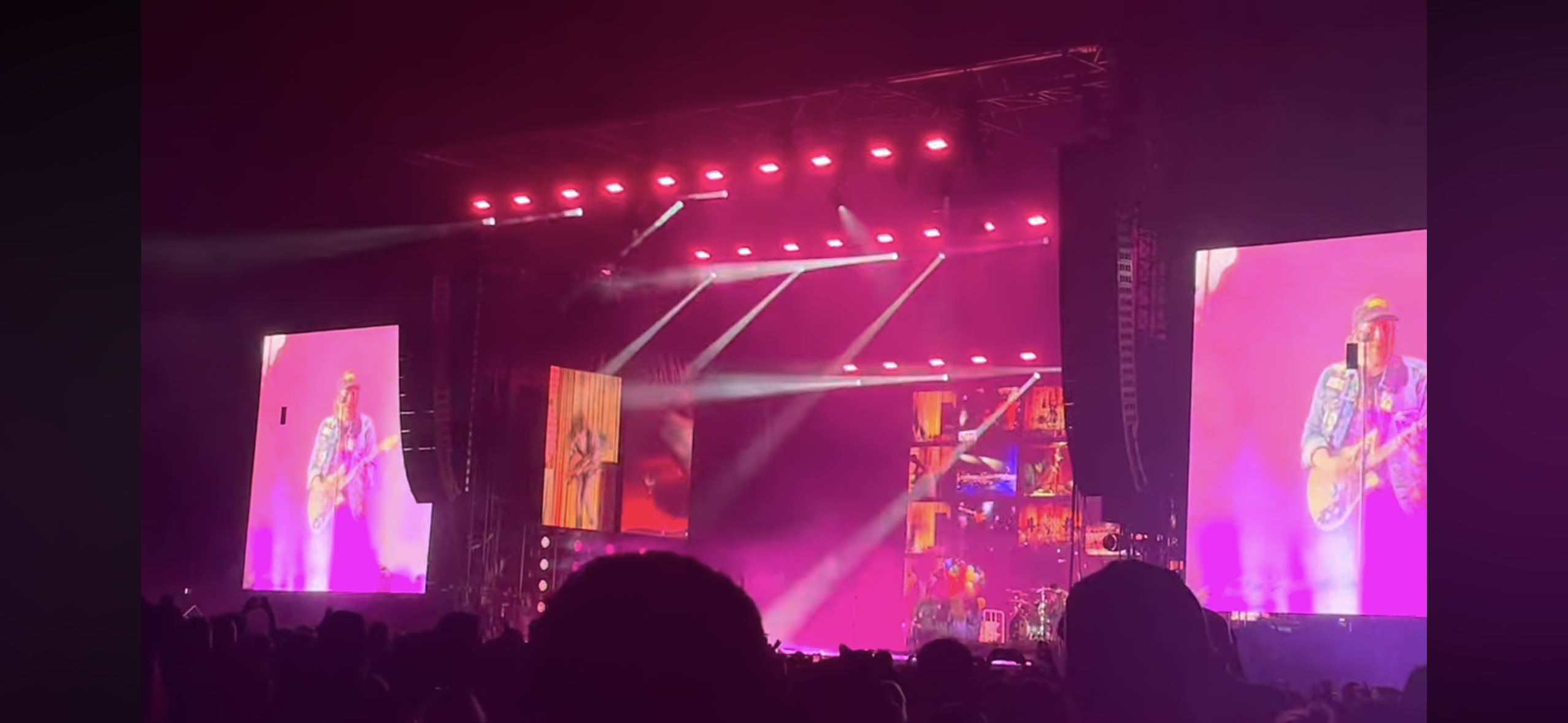 a concert featuring a band playing live on stage with the frontman holding a guitar. the stage is brightly lit and the crowd is cheering.