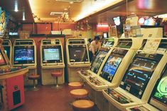 the image shows the interior of a brightly lit japanese arcade, filled with rows of classic arcade game cabinets.  a lone person is visible in the background, engrossed in a game. the atmosphere is lively and colorful, capturing the essence of retro gaming culture.