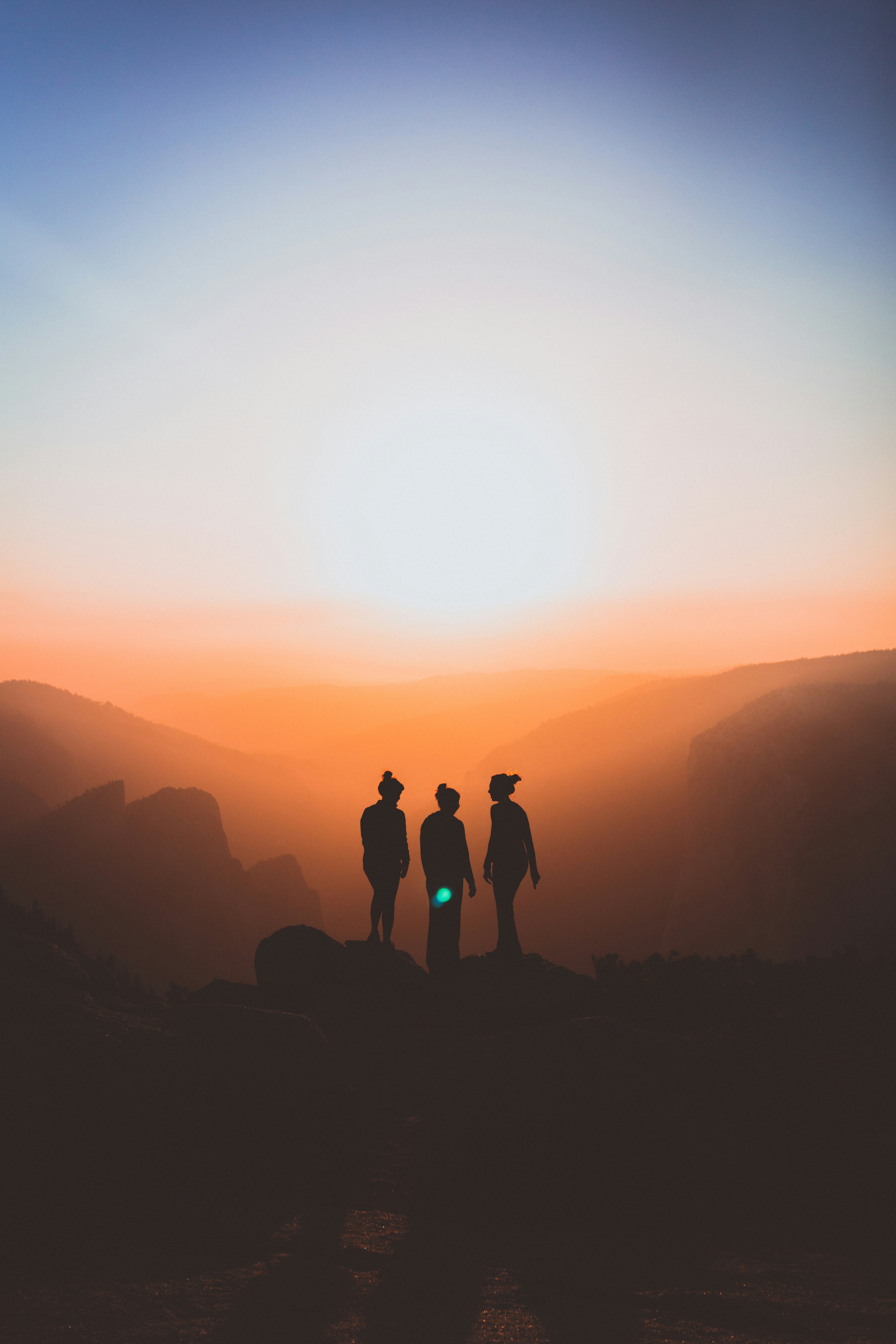 three people are silhouetted against a vibrant sunset. they are standing on a rock outcropping overlooking a mountain range. the sky is ablaze with warm colors, creating a sense of awe and wonder.