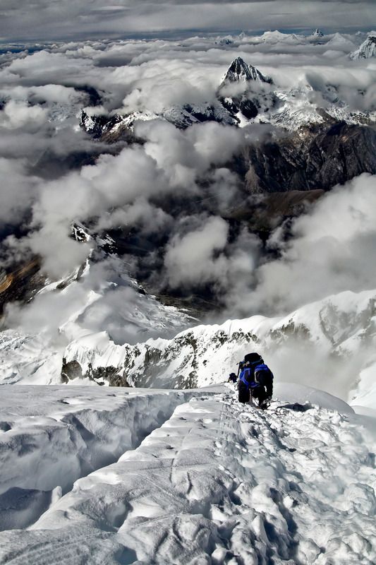 a lone climber ascends a snowy mountain peak. the climber is wearing a blue jacket and is dwarfed by the vastness of the snowcovered landscape. the summit is shrouded in clouds, making the climb even more challenging. the image captures the beauty and the danger of mountain climbing.