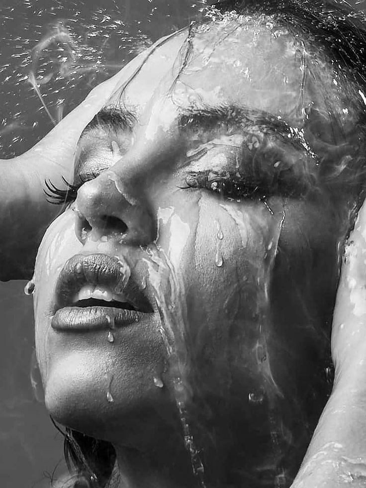 the image is a closeup, black and white portrait of a woman's face partially submerged in water. water is dripping from her hair and face, creating a dramatic and sensual effect. her eyes are closed, and her expression is serene and peaceful. the overall mood is artistic and elegant, highlighting the beauty of the woman and the textural qualities of the water. the contrast between the smooth skin and the dynamic water creates visual interest.