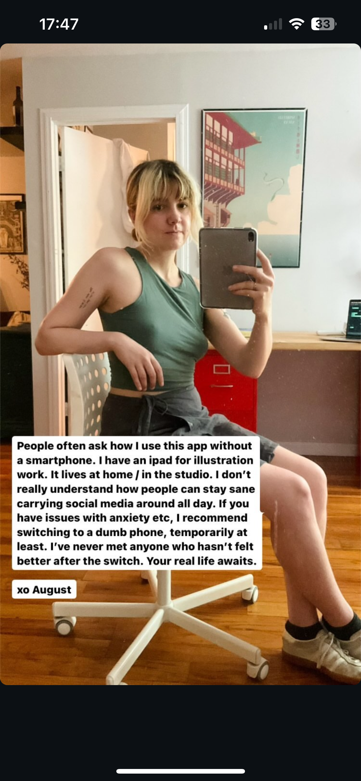 a young woman with short blonde hair and tattoos is taking a mirror selfie. she's wearing a black tank top and black pants. she's holding a black smartphone in front of her face, partially obscuring it. the background of the photo is a white wall with a framed picture on it. the image has text overlaid on it, discussing the use of smartphones and social media, and the benefits of switching to a "dumb phone".