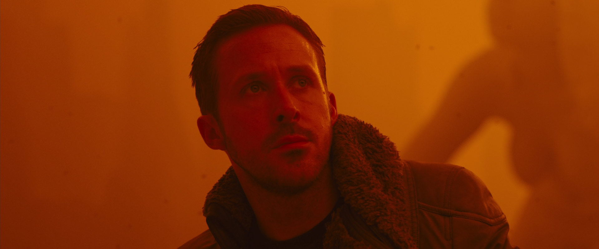 a man with short hair and a goatee looks up with a serious expression. the lighting is warm and orange, creating a futuristic and cyberpunk atmosphere. the man is wearing a dark jacket with a fur collar.