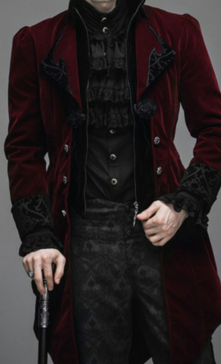 a man is shown from the midchest down wearing a burgundy velvet coat, a black dress shirt with ruffles, and dark dress pants. the coat has black gothicstyle detailing around the lapels and cuffs. the man is holding a cane in his left hand. the overall style is gothic or vampireinspired.
