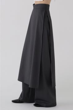 a woman is wearing a black skirt that is layered over pants. it is high waisted and long, flowing with a dress like appearance.  she is standing with her feet together and is wearing black high heels.  the skirt is very elegant and formal, and the woman is dressed in a fashionable style.
