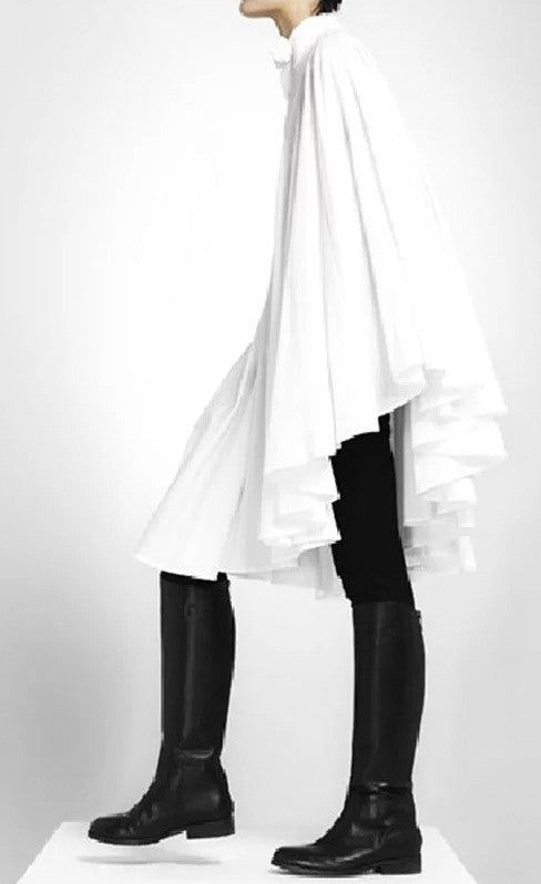 a model stands in a studio wearing a white cape, black leggings, and black boots. they are positioned against a white background. the cape is flowing and has multiple layers.