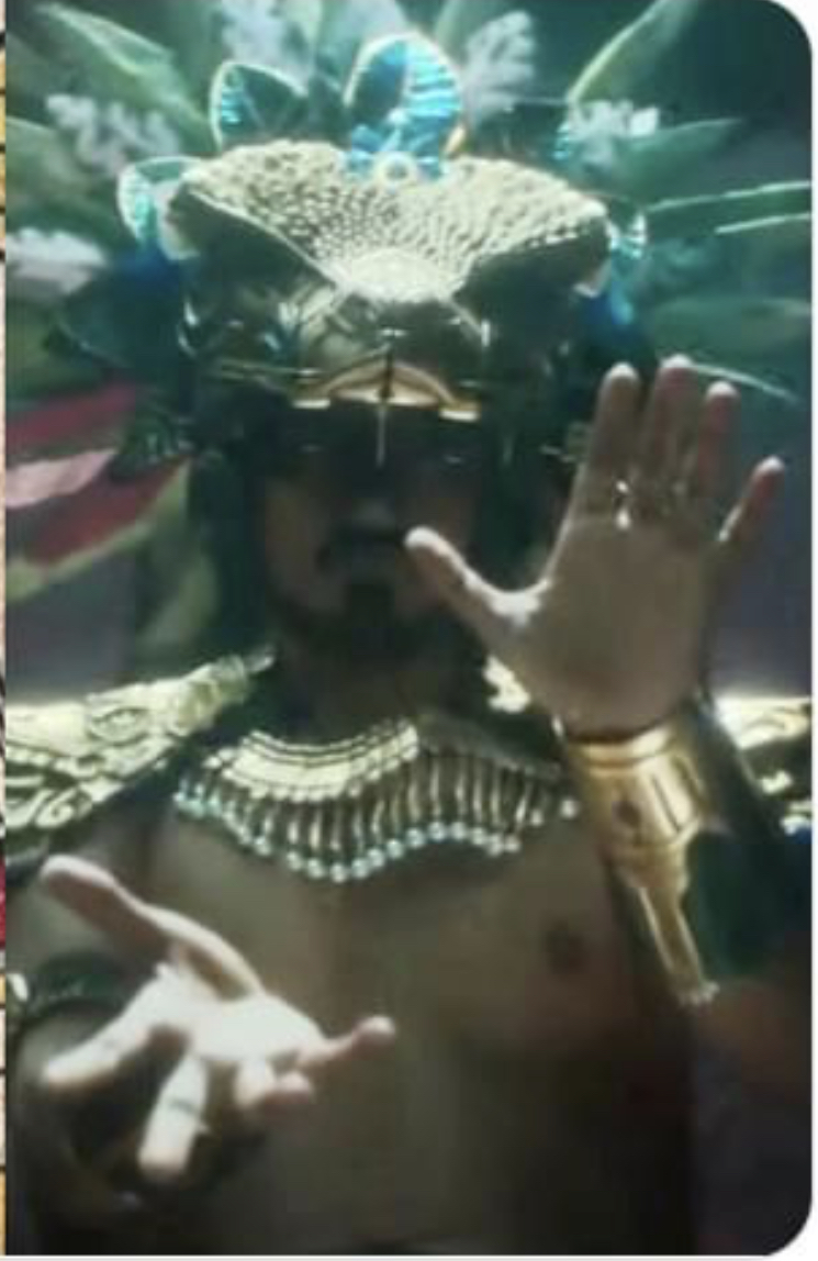 a man, adorned in elaborate aztecinspired ceremonial garb, dominates the frame. his headdress, a magnificent golden serpent, obscures his upper face, drawing attention to his intense gaze emanating from beneath the mask. his outstretched hands, palms open, suggest a ritualistic pose, further emphasizing the mystical aura surrounding him.  the lighting, reminiscent of stage spotlights, casts dramatic shadows, amplifying the mystique and emphasizing the intricate details of his attire.