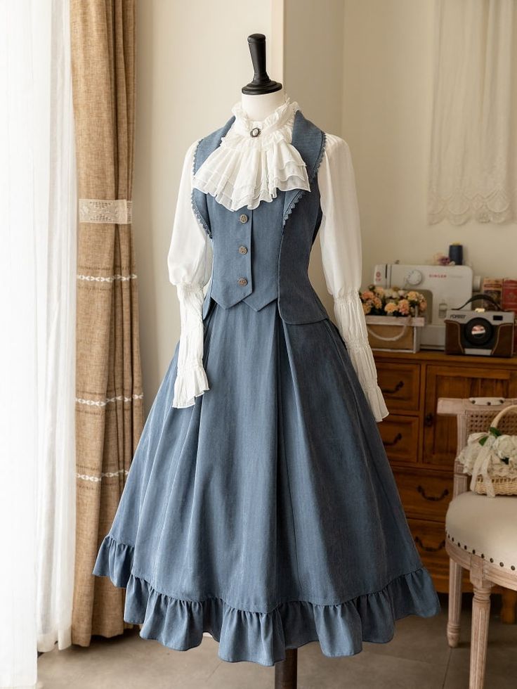 a blue vintagestyle lolita fashion dress is shown on a mannequin. the dress has a white blouse underneath and is a long dress with ruffles on the skirt. the dress is in a room with a white curtain in the background.