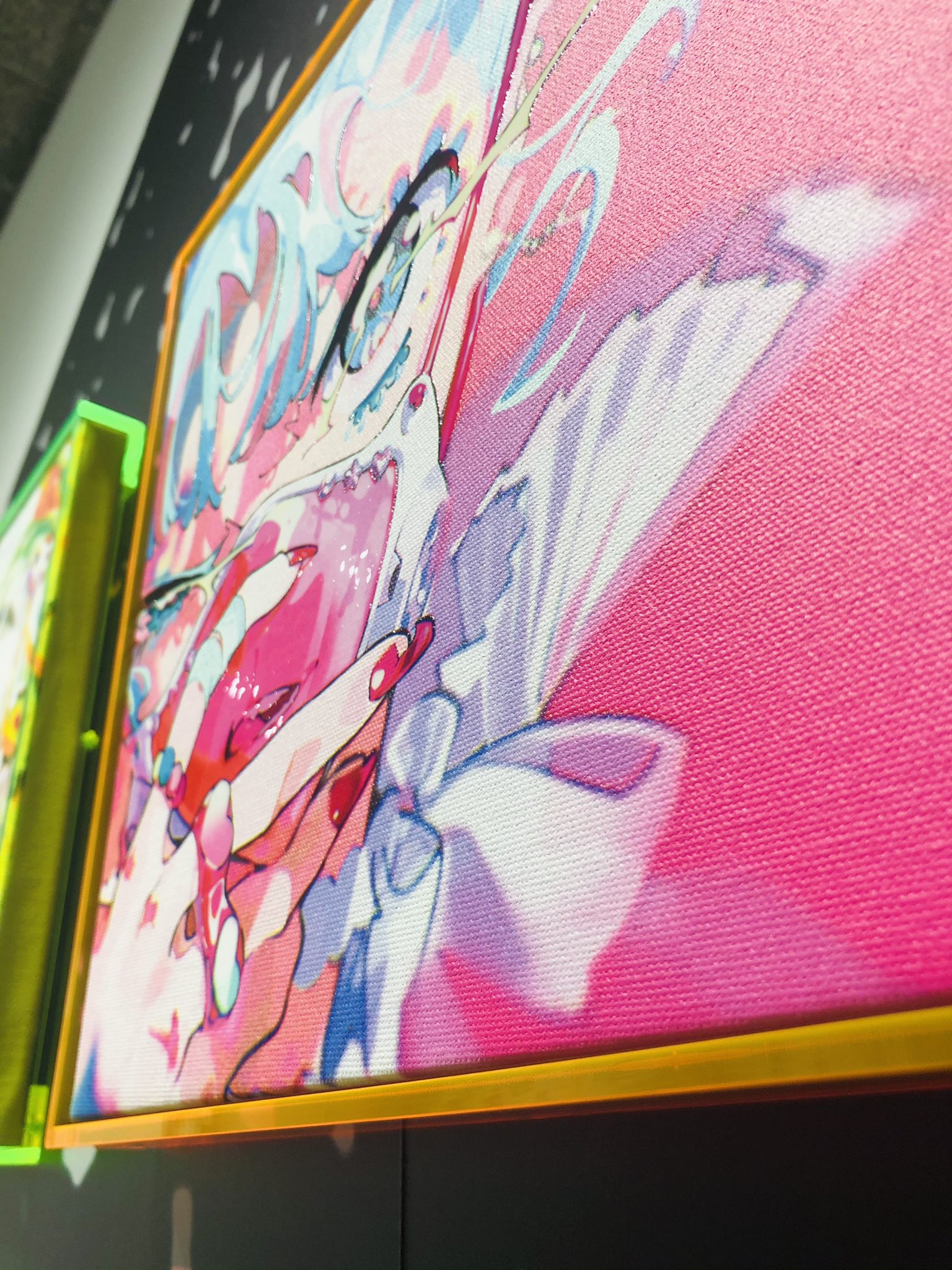 a closeup shot of a colorful pop art painting of a woman with blue hair and a pink bow on her shirt. the painting is framed with a neon orange frame and displayed in an art gallery. the background features a dark wall and another artwork with a green neon frame.