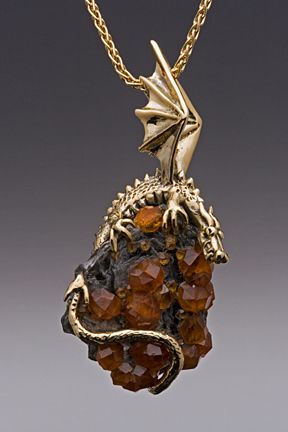 a closeup studio shot of a gold pendant in the shape of a dragon perched on a cluster of orange stones or crystals, suspended from a gold chain.