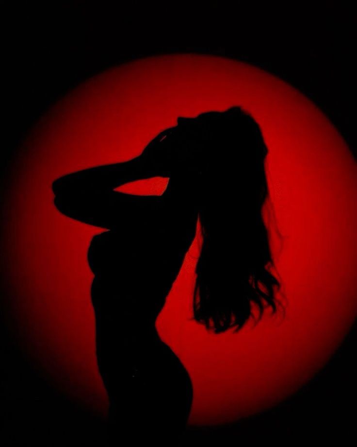a silhouette of a woman with long, flowing hair, standing in front of a red background. the woman's pose is mysterious and sensual. her hair is styled in a long, flowing manner that adds to the overall mystique of the image.