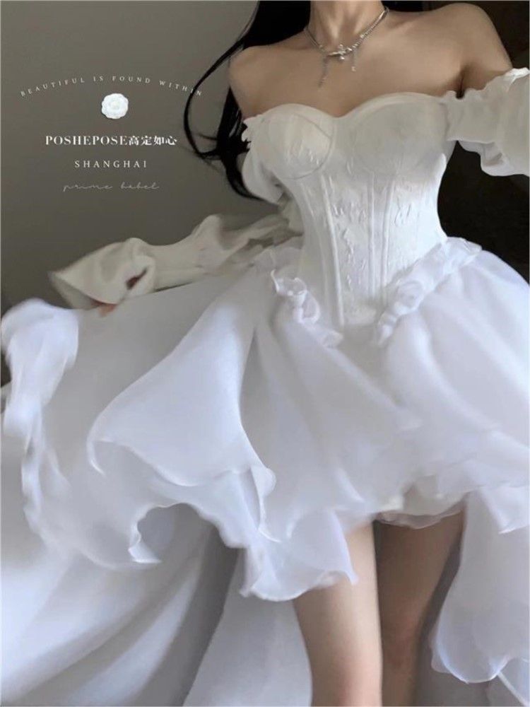 a woman is wearing a white, offtheshoulder dress with a corset bodice and ruffled chiffon skirt. she is also wearing a silver necklace.