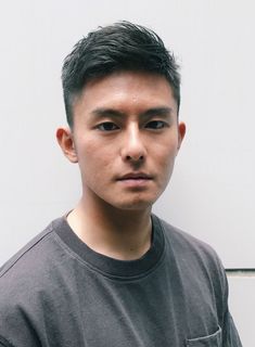 a young asian man with short, dark hair styled in a crew cut poses for a headshot against a neutral background. he is wearing a dark gray tshirt and has a neutral expression on his face. the lighting is soft and diffused, creating a natural and approachable look.