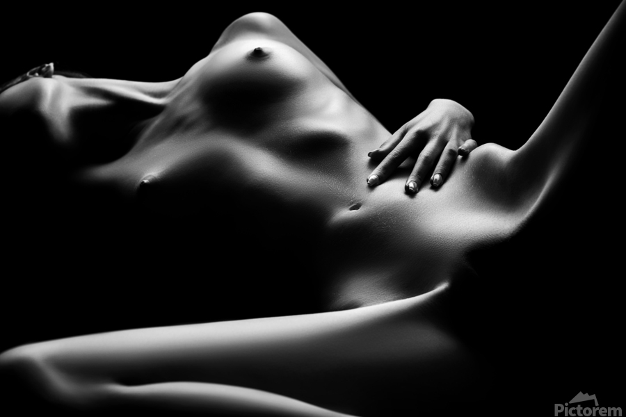 the image is a black and white, closeup photograph of a nude female body. the woman is lying down, her body positioned diagonally across the frame.  the lighting is dramatic, using chiaroscuro to highlight the curves and contours of her body, creating strong contrasts between light and shadow. the focus is on the textures and forms of the body, with little detail visible beyond the smooth skin and musculature. the overall mood is sensual and intimate, and the style leans towards fine art photography. the woman's hand rests gently on her lower abdomen.