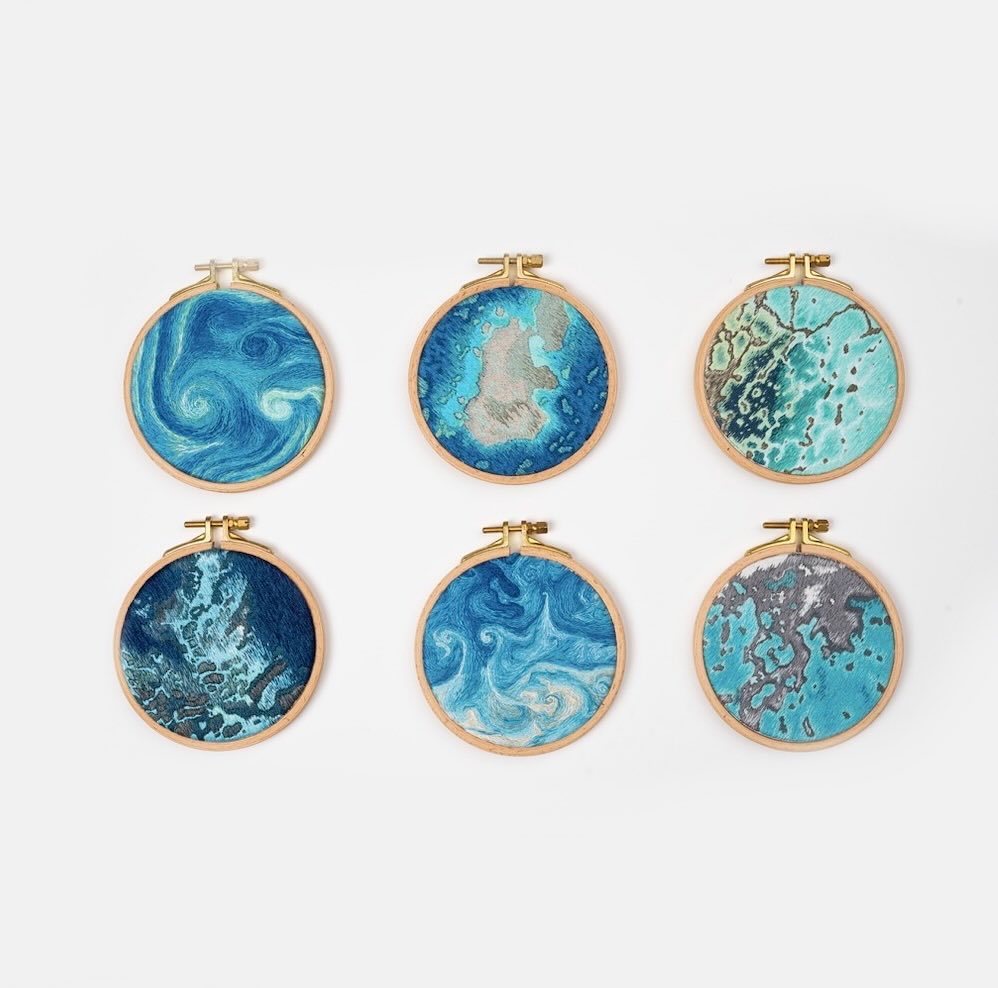 the image shows six embroidery hoops arranged in two rows of three. each hoop holds a piece of fabric with an abstract design resembling water or waves, primarily in shades of blue and green. they are displayed against a clean white background.