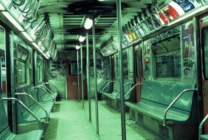 he image shows the interior of a vintage subway car, heavily adorned with graffiti. the seats are metallic green and worn, with a general sense of age and disuse.  the overall color palette is muted green, contributing to a grunge aesthetic.  the car is mostly empty, and the lighting is dim, highlighting the graffiti and the wear and tear on the subway car's interior.  the scene suggests a gritty, urban environment, possibly in new york city, during the 1980s or 1990s.
