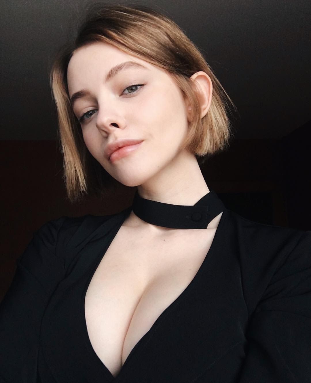a beautiful blonde woman with short hair is wearing a black dress with a choker necklace. she is looking at the camera. she is posed in a studio setting.