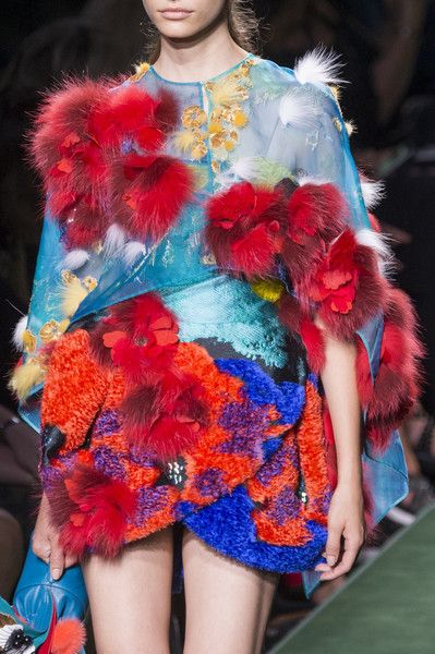 this image features a highfashion model showcasing a stunning couture dress on a runway. the dress is a vibrant explosion of color and texture, with fur, embroidery, lace, and bold patterns that create a striking visual effect. the model's confident pose and glamorous makeup enhance the drama of the outfit, making this an unforgettable fashion moment.